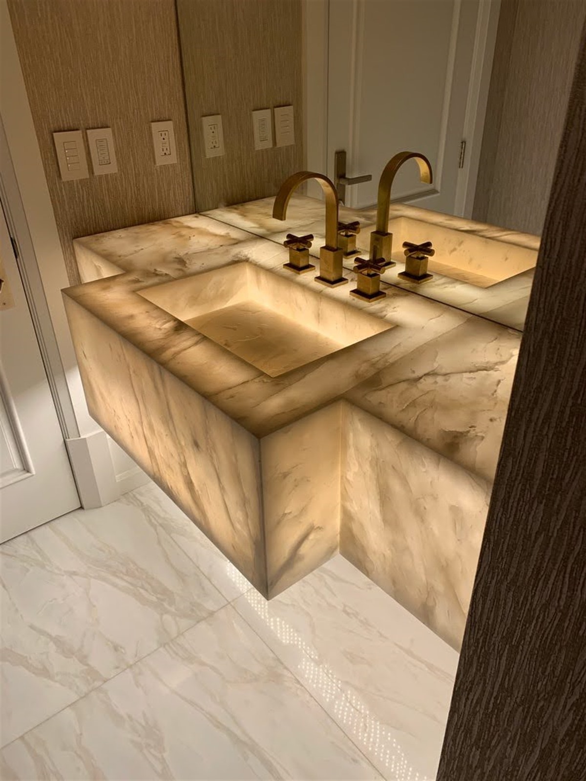 Backlit onyx vanity with carved sink basin and brushed-brass fixtures by LIT Group, high-end residential project in Los Angeles.